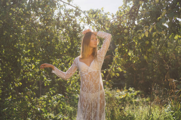 Young beautiful girl in white lace dress in apple garden