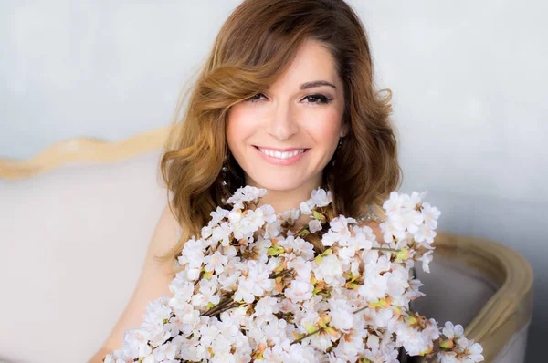 Portrait of smiling beautiful young woman with bouquet of white sakura in hands