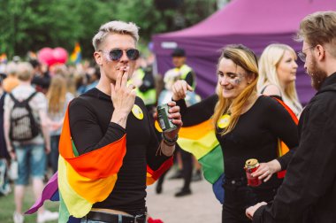 İnsanlar Helsinki Pride'da piknikte sigara içip bira içiyor.