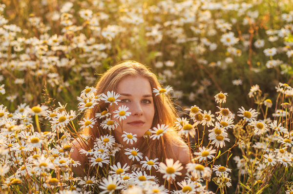 Portrait of pretty blond woman sitting in chamomile field