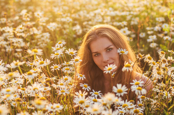 Portrait of pretty blond woman sitting in chamomile field