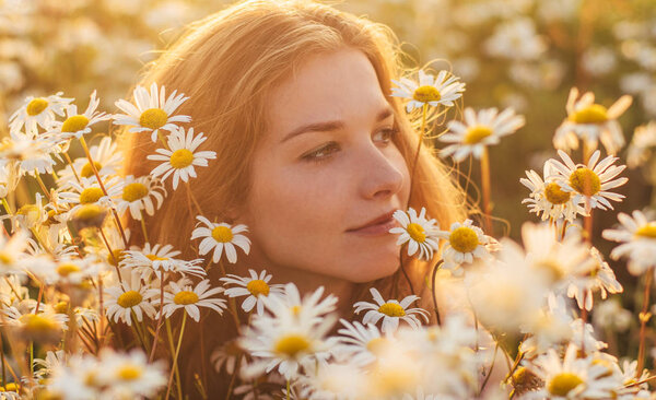 Portrait of pretty and smiling  blond woman sitting in chamomile