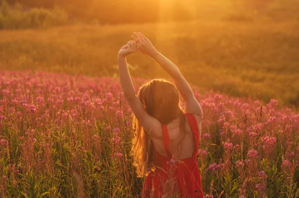 Девушка в красном платье сидит сзади с поднятыми руками среди цветущих S — стоковое фото
