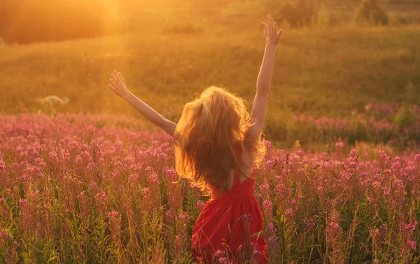 Çiçekler arasında kırmızı elbiseli, dans eden ve zıplayan kız. — Stok fotoğraf