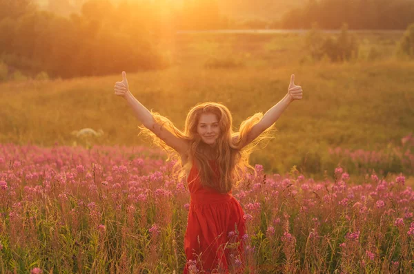 Bailando y saltando chica con pulgares arriba en vestido rojo entre la floración — Foto de Stock