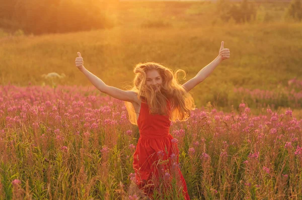 Bailando y saltando chica con pulgares arriba en vestido rojo entre la floración —  Fotos de Stock