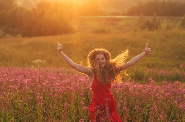 Bailando y saltando chica con pulgares arriba en vestido rojo entre la floración —  Fotos de Stock