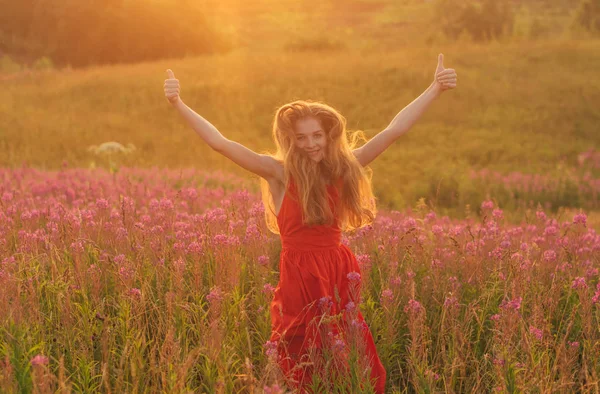Bailando y saltando chica con pulgares arriba en vestido rojo entre la floración —  Fotos de Stock