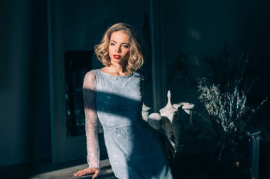 Kaliteli makyajlı ve saç stili güzel sarışın kız aynanın yanında, yüzünde güneşli ışınlar var.