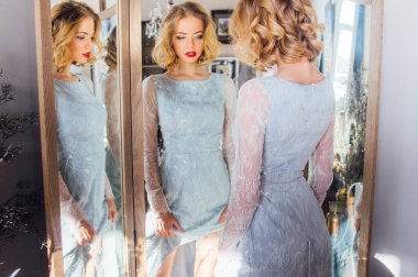 Klasik makyajlı ve saç stili güzel sarışın kız üçlü aynanın yanında duruyor.