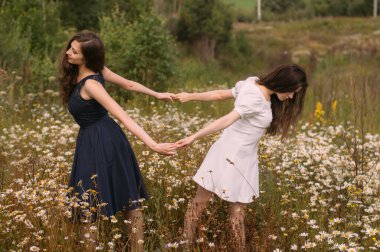 Papatya tarlasında dans eden ve el ele tutuşan iki kız.