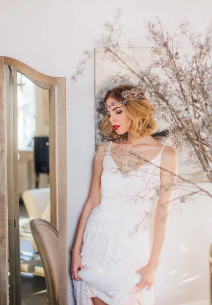 Kaliteli makyajlı, saç stili ve kapalı gözlü güzel sarışın kız aynanın yanında elinde elbiseyle duruyor.