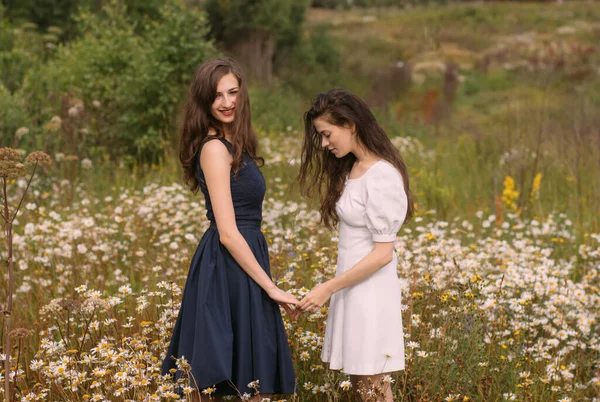 Papatya tarlasında dikilen iki kız doğada ve el ele tutuşuyorlar.