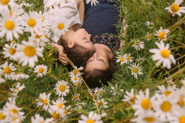 Güneşli bir günde koyu mavi ve beyaz elbiseli iki kız uzanıp papatya tarlasında doğada uyuyor.