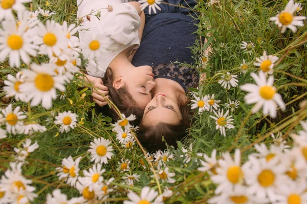 Güneşli bir günde koyu mavi ve beyaz elbiseli iki kız uzanıp papatya tarlasında doğada uyuyor.