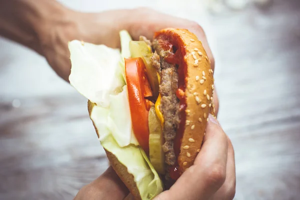 Hands holding fresh delicious burger on the wooden table top view.