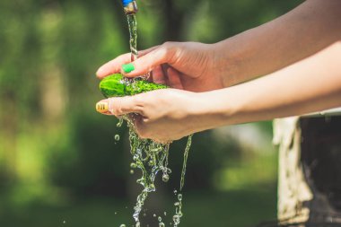 Bahçe arka planda su sıçraması ile kadın elinde salatalık yıkama