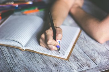 Çeşitli eşyalarla ahşap masaüstüne yerleştirilen not defterine yazı yazan kadın ellerinin kapatılması
