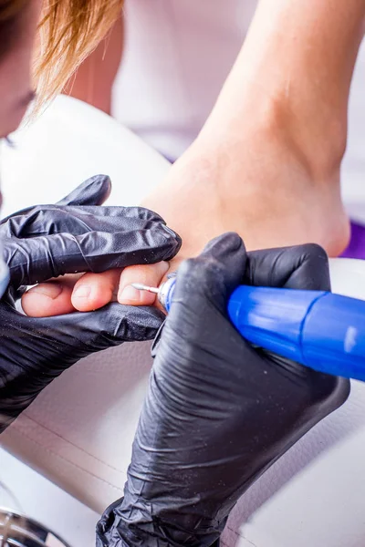 Mestre de pedicure durante o trabalho. Close-up de pés femininos e mãos em luvas com uma máquina-ferramenta especial . — Fotografia de Stock