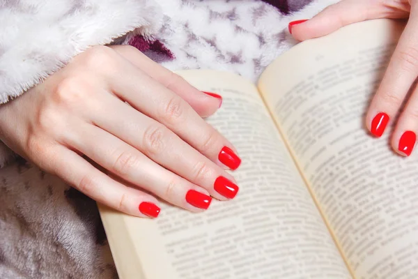 Jonge meisjes handen met rode nagels houden van een boek. Onherkenbaar vrouw met mode-manicure in retro deken lezen boek. Close-up — Stockfoto