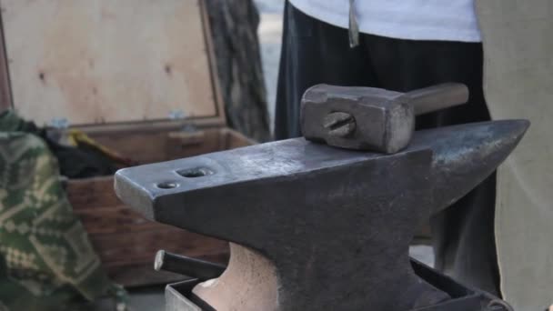 En la industria un herrero, trabajando hierro caliente golpeándolo con un martillo en yunque, y causa chispas calientes. Detrás del herrero un trabajador usando la máquina de soldadura . — Vídeos de Stock