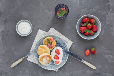 Süzme peynir kahvaltı veya gri arka plan üzerinde öğle yemeği için ekşi krema ve çilek ile krep. Sağlıklı gıda kavramı. Yukarıda