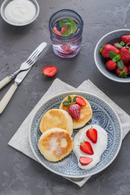 Süzme peynir kahvaltı veya gri arka plan üzerinde öğle yemeği için ekşi krema ve çilek ile krep. Sağlıklı gıda kavramı. Yukarıda