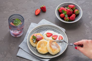 Süzme peynir kahvaltı veya gri arka plan üzerinde öğle yemeği için ekşi krema ve çilek ile krep. Sağlıklı gıda kavramı. Kadın eli bir çatal tutan. 