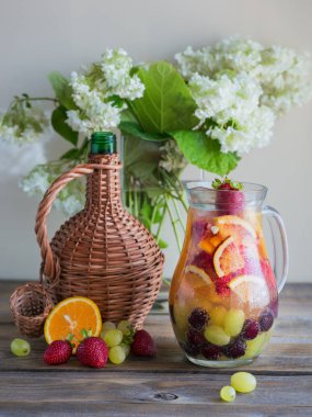 Geleneksel yaz içki beyaz köpüklü şarap sangria. Ev yapımı serinletici meyve sangria veya şampanya, çilek, portakal ve üzüm yumrukla. Bir ahşap rustik masa üzerinde bir sürahi ve malzemeler ile