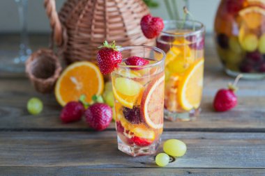 Geleneksel yaz içki beyaz köpüklü şarap sangria. Ev yapımı serinletici meyve sangria veya şampanya, çilek, portakal ve üzüm yumrukla. Bir sürahi ve malzemeler üzerinde ahşap rustik masa