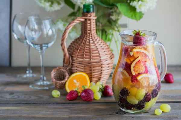 Geleneksel yaz içki beyaz köpüklü şarap sangria. Ev yapımı serinletici meyve sangria veya şampanya, çilek, portakal ve üzüm yumrukla. Bir ahşap rustik masa üzerinde bir sürahi ve malzemeler ile
