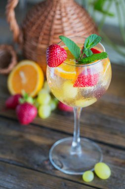 Geleneksel yaz içki beyaz köpüklü şarap sangria. Ev yapımı serinletici meyve sangria veya şampanya, çilek, portakal ve üzüm yumrukla gözlük ve malzemeler ahşap rustik tablo