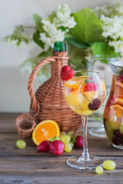 Geleneksel yaz içki beyaz köpüklü şarap sangria. Homemade Meyve sangria şampanya, çilek, portakal ve üzüm ile yenileniyor. Bir sürahi ve malzemeler ile ahşap rustik masaya