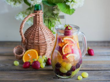Geleneksel yaz içki beyaz köpüklü şarap sangria. Ev yapımı serinletici meyve sangria veya şampanya, çilek, portakal ve üzüm yumrukla. Bir ahşap rustik masa üzerinde bir sürahi ve malzemeler ile