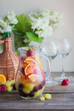 Geleneksel yaz içki beyaz köpüklü şarap sangria. Ev yapımı serinletici meyve sangria veya şampanya, çilek, portakal ve üzüm yumrukla. Bir ahşap rustik masa üzerinde bir sürahi ve malzemeler ile