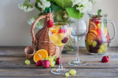 Geleneksel yaz içki beyaz köpüklü şarap sangria. Homemade Meyve sangria şampanya, çilek, portakal ve üzüm ile yenileniyor. Bir sürahi ve malzemeler ile ahşap rustik masaya