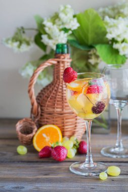 Geleneksel yaz içki beyaz köpüklü şarap sangria. Homemade Meyve sangria şampanya, çilek, portakal ve üzüm ile yenileniyor. Bir sürahi ve malzemeler ile ahşap rustik masaya
