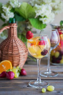 Geleneksel yaz içki beyaz köpüklü şarap sangria. Homemade Meyve sangria şampanya, çilek, portakal ve üzüm ile yenileniyor. Bir sürahi ve malzemeler ile ahşap rustik masaya