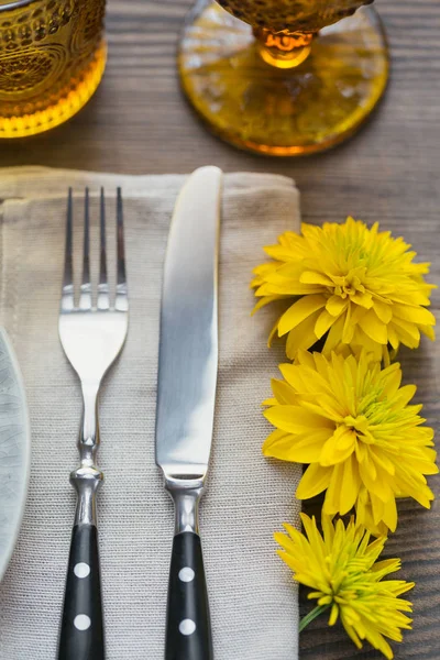Rustic table setting with linen napkin, cutlery, ceramic plates, yellow glasses and yellow flowers on dark wooden table. Holiday table decoration. Romantic dinner.