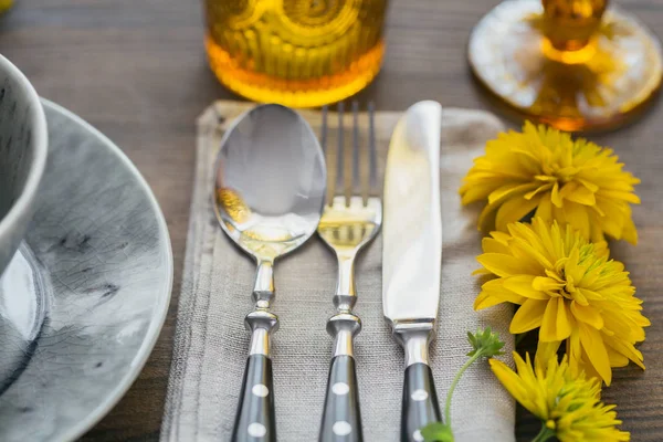 Rustic table setting with linen napkin, cutlery, ceramic plates, yellow glasses and yellow flowers on dark wooden table. Holiday table decoration. Romantic dinner.