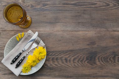 Rustik sofra keten peçete, çatal bıçak takımları, seramik kaplamalar, sarı gözlük ve koyu ahşap masaya sarı çiçek. Tatil masa dekorasyonu. Romantik bir akşam yemeği.