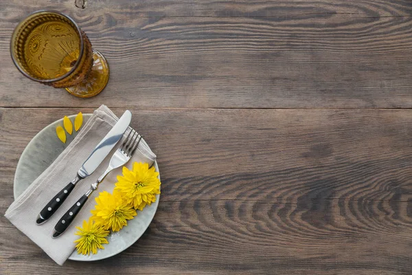 Rustik sofra keten peçete, çatal bıçak takımları, seramik kaplamalar, sarı gözlük ve koyu ahşap masaya sarı çiçek. Tatil masa dekorasyonu. Romantik bir akşam yemeği.