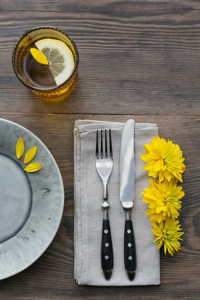 Rustik sofra keten peçete, çatal bıçak takımları, seramik kaplamalar, sarı gözlük ve koyu ahşap masaya sarı çiçek. Tatil masa dekorasyonu. Romantik bir akşam yemeği.
