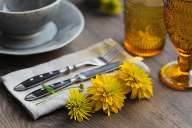 Rustik sofra keten peçete, çatal bıçak takımları, seramik kaplamalar, sarı gözlük ve koyu ahşap masaya sarı çiçek. Tatil masa dekorasyonu. Romantik bir akşam yemeği.