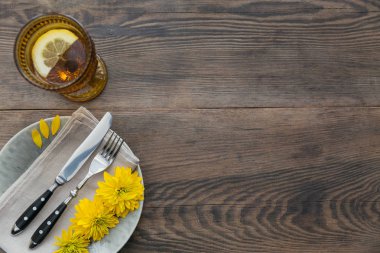 Rustik sofra keten peçete, çatal bıçak takımları, seramik kaplamalar, sarı gözlük ve koyu ahşap masaya sarı çiçek. Tatil masa dekorasyonu. Romantik bir akşam yemeği.
