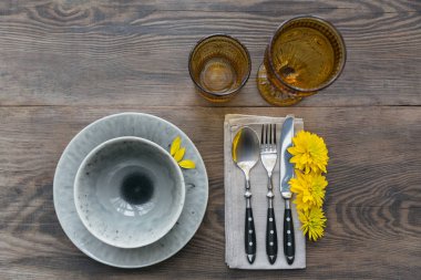 Rustik sofra keten peçete, çatal bıçak takımları, seramik kaplamalar, sarı gözlük ve koyu ahşap masaya sarı çiçek. Tatil masa dekorasyonu. Romantik bir akşam yemeği.
