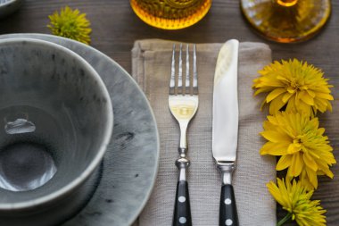 Rustik sofra keten peçete, çatal bıçak takımları, seramik kaplamalar, sarı gözlük ve koyu ahşap masaya sarı çiçek. Tatil masa dekorasyonu. Romantik bir akşam yemeği.