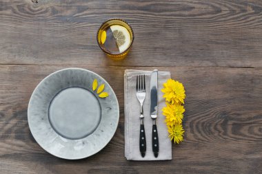 Rustik sofra keten peçete, çatal bıçak takımları, seramik kaplamalar, sarı gözlük ve koyu ahşap masaya sarı çiçek. Tatil masa dekorasyonu. Romantik bir akşam yemeği.