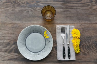 Rustik sofra keten peçete, çatal bıçak takımları, seramik kaplamalar, sarı gözlük ve koyu ahşap masaya sarı çiçek. Tatil masa dekorasyonu. Romantik bir akşam yemeği.