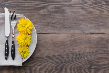 Rustik sofra keten peçete, çatal bıçak takımları, seramik kaplamalar, sarı gözlük ve koyu ahşap masaya sarı çiçek. Tatil masa dekorasyonu. Romantik bir akşam yemeği.
